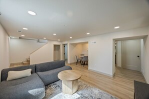 Ein modernes Wohnzimmer mit einem grauen Sofa, einem runden Couchtisch und einem Essbereich mit kleinem Tisch und Stühlen.