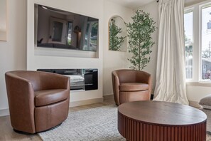 Ein Wohnzimmer mit Kamin, zwei Ledersesseln, einem runden Couchtisch und einem großen Spiegel an der Wand.