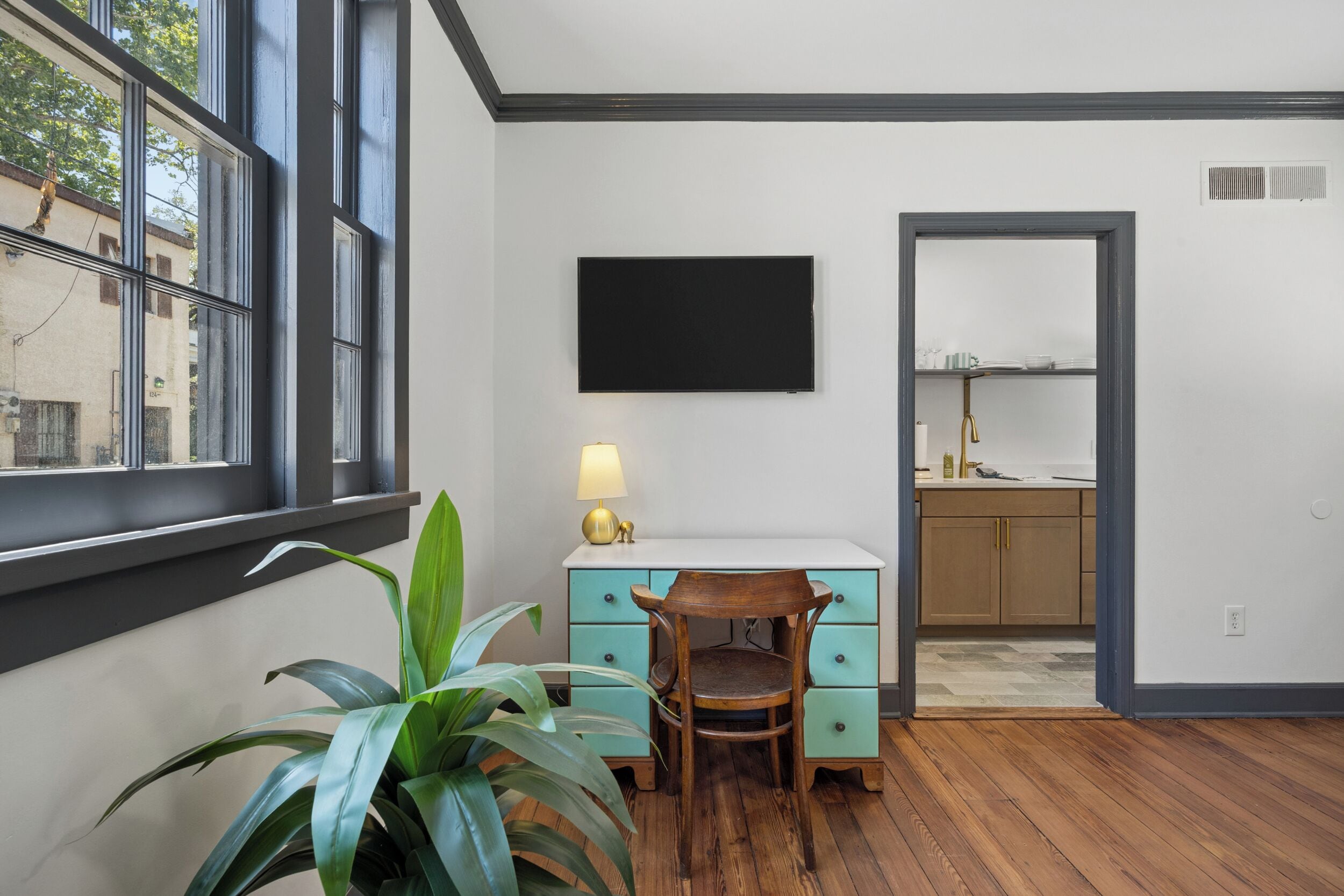 A room with a desk, chair, potted plant, and a TV mounted on the wall.