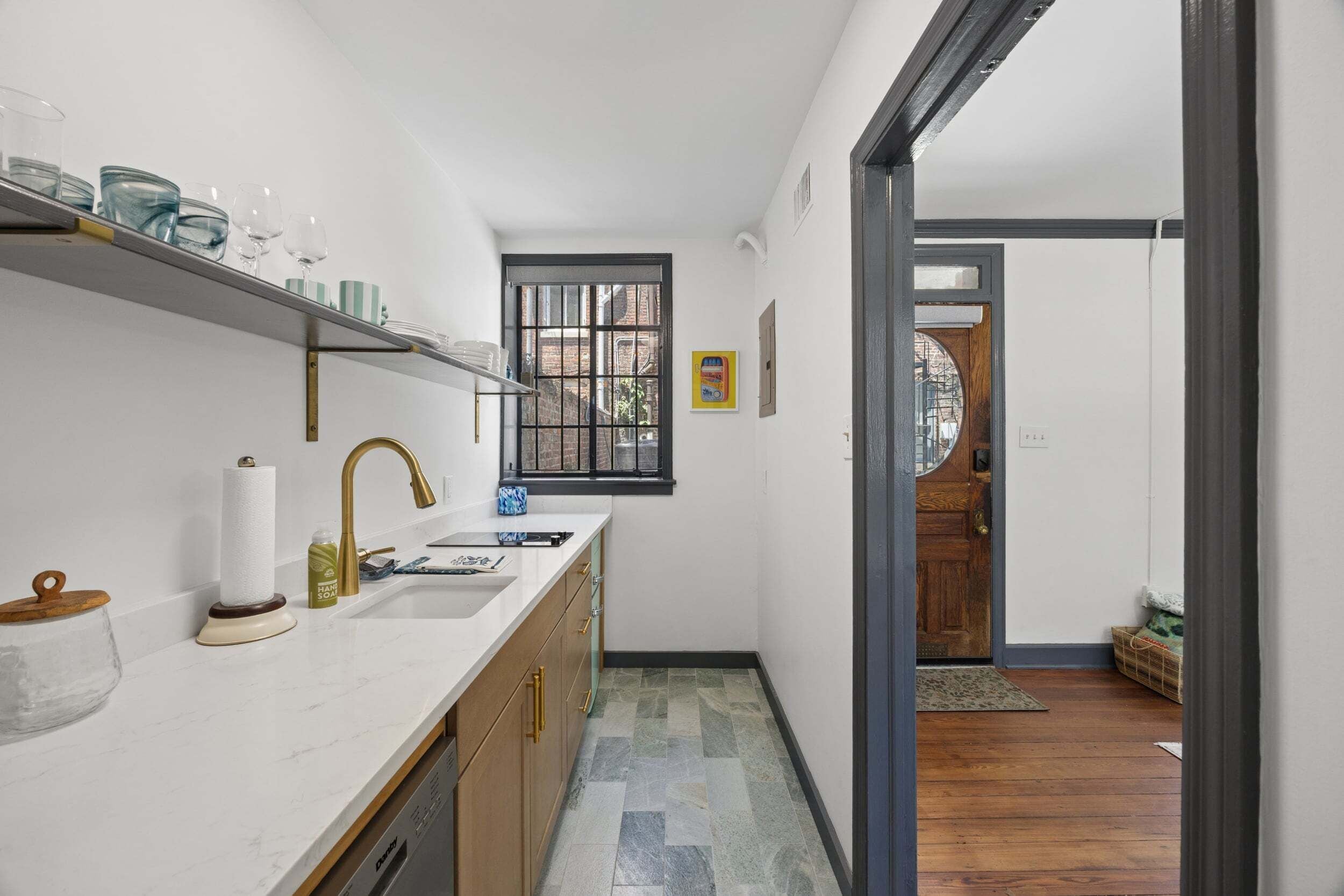 A narrow kitchen with a white countertop, a gold faucet, and a window with bars.