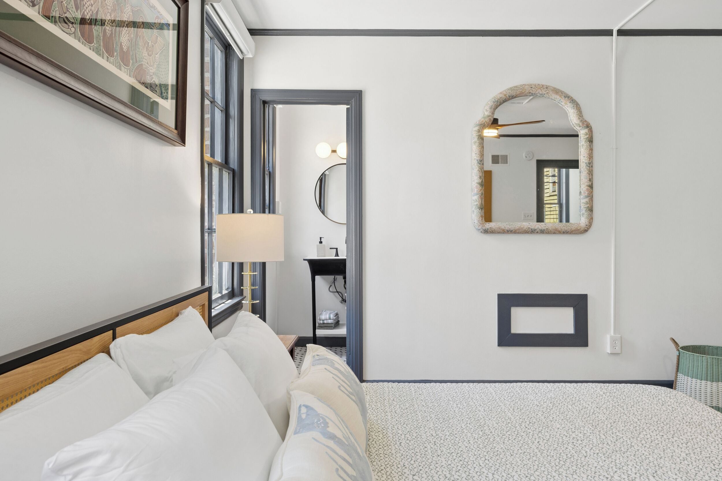 A hotel room with a bed, a bedside table, a mirror, and a wall-mounted picture frame.