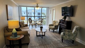 A living room with a sofa, armchairs, a coffee table, a TV, and a dining area with chairs and a table. - Magnolia Moments (Biloxi)