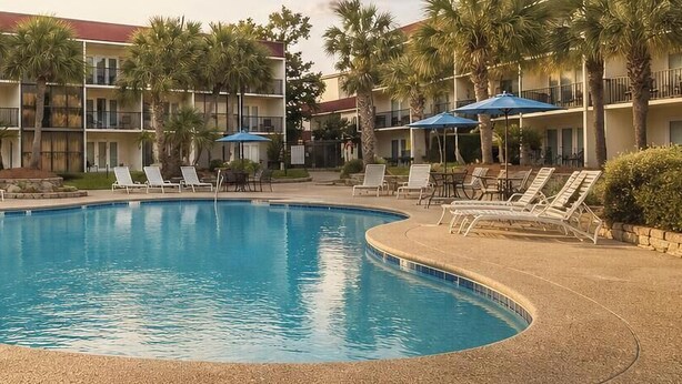 A swimming pool with lounge chairs and umbrellas, surrounded by a multi-story building with balconies. - Magnolia Moments (Biloxi)