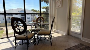 A dining area with a glass table, four chairs, a decorative plate, and a view of a residential area through large windows. - Magnolia Moments (Biloxi)