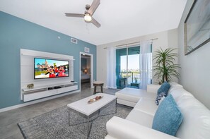 Ein Wohnzimmer mit Fernseher, weißem Sofa, Couchtisch und Deckenventilator.