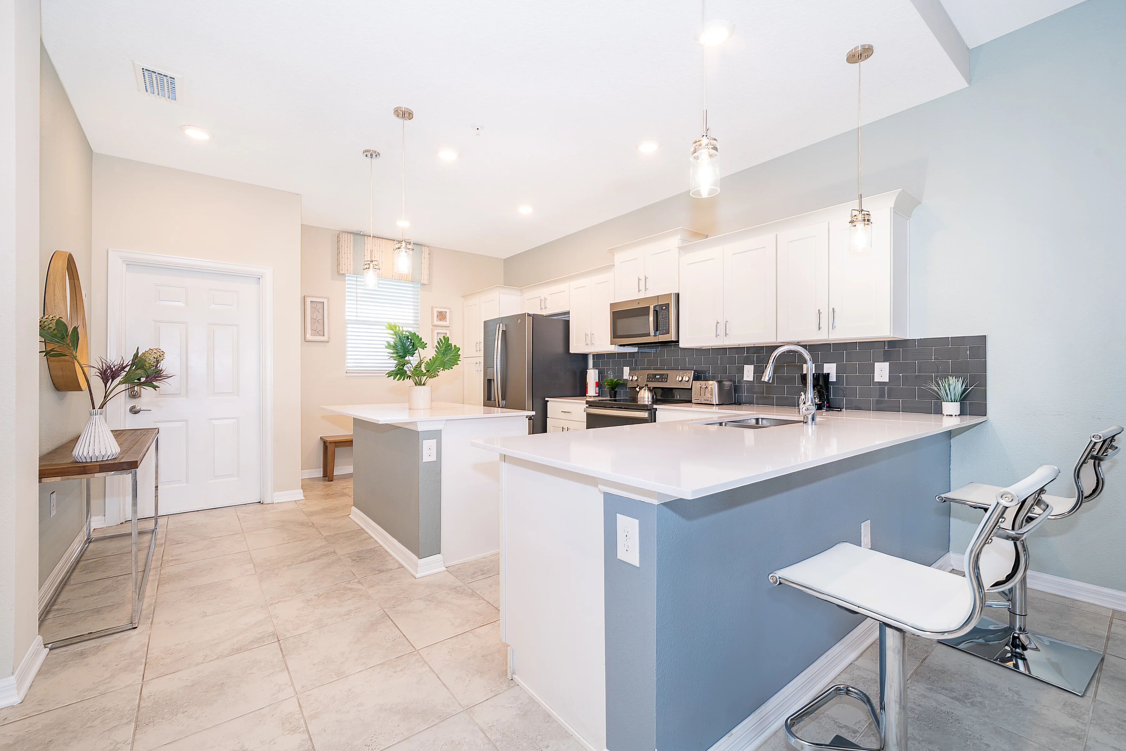 A modern kitchen with white cabinets, a central island, stainless steel appliances, and pendant lighting.