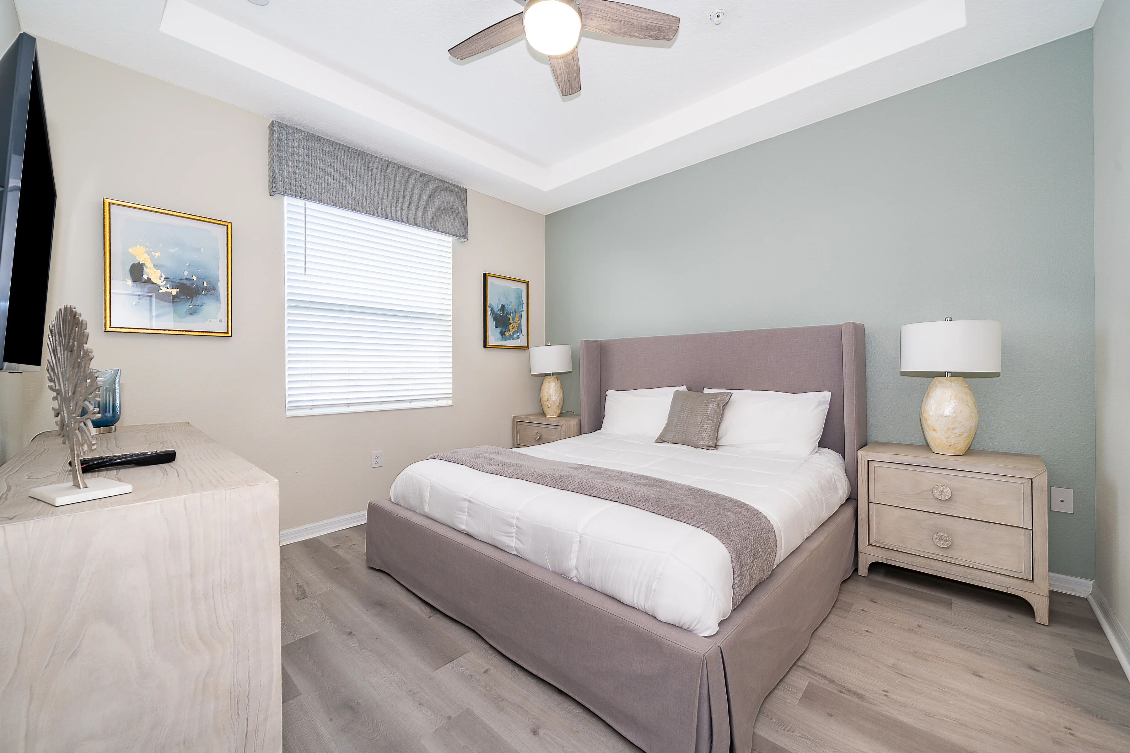 Ein Schlafzimmer mit Bett, Nachttischen, Deckenventilator, Kunstwerken und einem Schreibtisch mit Lampe.