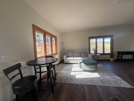 A living room with a sofa, ottoman, dining table, chairs, and large windows with a view.. Private studio at Bayou Hills BnB in charming Parker perfect for getaway