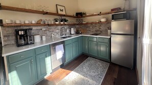 Una cucina con mobili color petrolio, un frigorifero in acciaio inossidabile, una macchina da caffè e un forno a microonde su una mensola di legno.