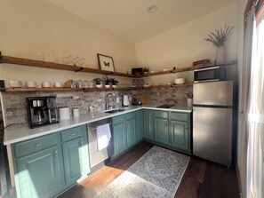 Una cocina con armarios azul verdosos, un refrigerador de acero inoxidable, una cafetera y un microondas sobre una repisa de madera.