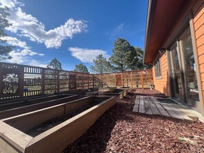 Eine Holzterrasse mit erhöhten Blumenbeeten, ein Holzzaun mit dekorativen Feldern und ein Gebäude mit großen Fenstern.