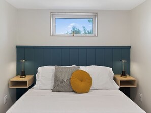 A bedroom with a bed, two bedside tables, a window, and a view of trees.