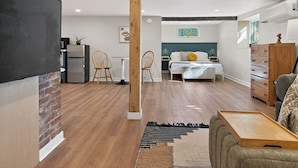 Una sala moderna con piso de madera, un sofá, una mesa de centro, un televisor montado en una pared de ladrillo y un comedor con sillas y una mesa.