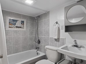 Une salle de bain avec une baignoire, des toilettes et un lavabo, dont le sol et les murs sont recouverts de carreaux de couleur claire, et un mur agrémenté d’un motif décoratif en carreaux.