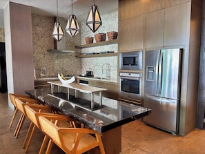 A modern kitchen with a central island, stainless steel appliances, and wooden chairs. - Spacious 4-Bedroom Grand Luxxe Retreat, Perfect for Families and Groups (Nuevo Vallarta)