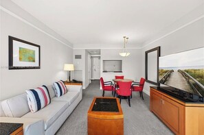 A modern hotel room with a sofa, dining table, chairs, a TV, and artwork on the walls. - Luxury Four Seasons One-Bedroom Suite in the Heart of Brickell. (Miami)