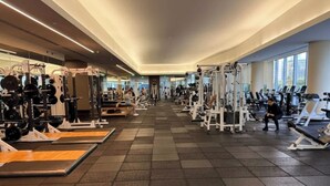 Ein Fitnessraum mit unterschiedlichen Trainingsgeräten, gefliestem Boden und großen Fenstern.