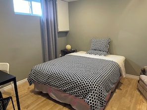 A bedroom with a bed, a nightstand, a chair, a table, and a window with curtains.