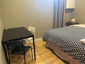 A room with a bed, a desk, a chair, and a small table with a lamp.
