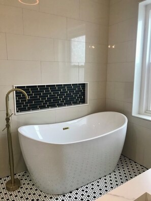 Ein modernes Badezimmer mit einer freistehenden Badewanne, einem goldenen Wasserhahn und einer schwarz-weißen Fliesenwand.