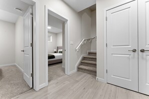 A hallway with carpeted flooring, white walls, and a staircase leading to a bedroom with a bed and a nightstand. - The Nook - 20 mins from airport | Games | Coffee (Edmonton)