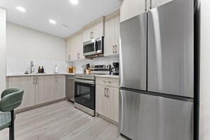 A modern kitchen with stainless steel appliances, wooden cabinets, and a green chair. - The Nook - 20 mins from airport | Games | Coffee (Edmonton)