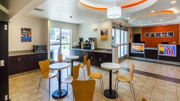 A modern restaurant with round tables and chairs, a kitchen area, and a counter with a digital display. - Days Inn by Wyndham South Bend /notre Dame (South Bend)