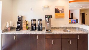 A hotel kitchen with coffee machines, a sink, and a sign for 'Rise & Shine'. - Days Inn by Wyndham South Bend /notre Dame (South Bend)