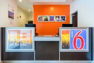 Un mostrador de recepción de hotel con una pared naranja, cuadros enmarcados y un letrero que indica que es un Motel 6.