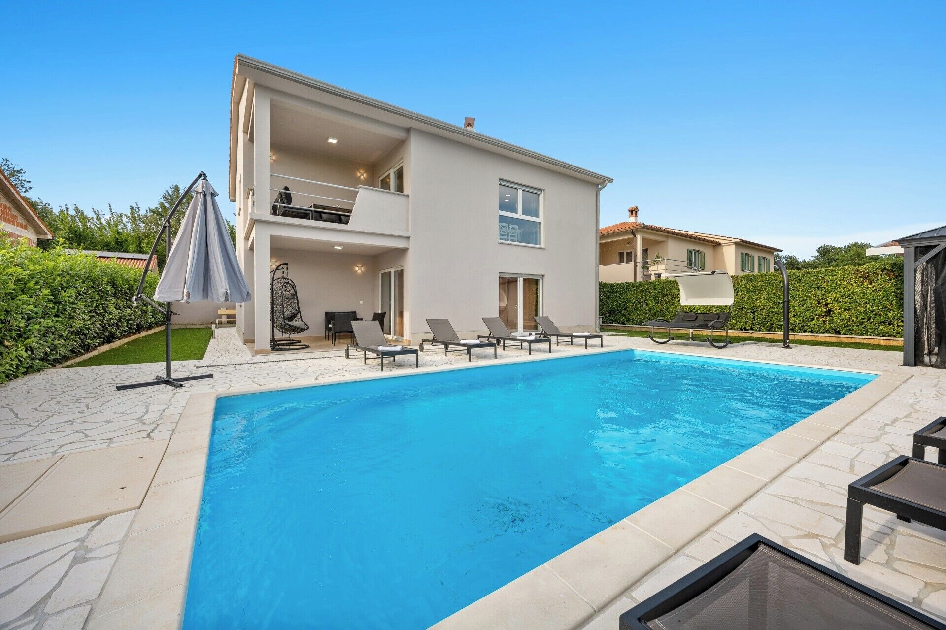 A modern two-story house with a swimming pool, outdoor seating, and a covered patio area.
