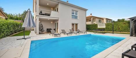 A modern two-story house with a swimming pool, outdoor seating, and a covered patio area.