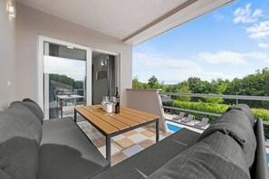 A balcony with a wooden table, two grey sofas, and a pool view. - Villa LanaB – Private Pool and Great Location by Istrabook (Labin)
