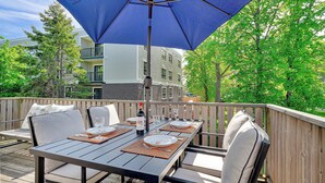 Une terrasse extérieure avec une table dressée pour le repas, un parasol bleu et une vue sur un bâtiment en arrière-plan.