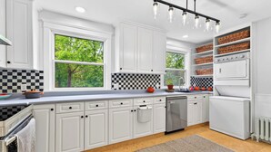 Une cuisine moderne avec des meubles blancs, un dosseret à carreaux et une vue sur la verdure à l’extérieur.