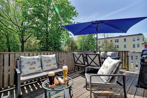 Una terraza con mobiliario exterior, una mesa con bebidas y un paraguas grande.