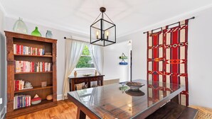 Un coin repas avec une table à plateau en verre, une bibliothèque en bois et un rideau à motifs.
