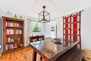 A dining area with a glass-top table, a wooden bookshelf, and a patterned curtain. - Bright second-floor home with private deck, modern kitchen, and calm style. (Charlottetown)