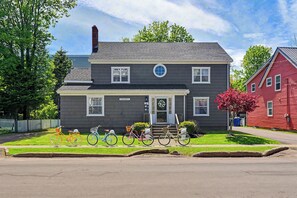 A two-story house with a front porch, a garage, and a red house adjacent to it. - Bright second-floor home with private deck, modern kitchen, and calm style. (Charlottetown)