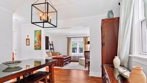 Un salon spacieux avec une table à manger en bois, un canapé et une table basse. On y trouve une grande fenêtre avec des rideaux, un meuble en bois et un luminaire suspendu.