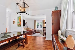 Un salon spacieux avec une table à manger en bois, un canapé et une table basse. On y trouve une grande fenêtre avec des rideaux, un meuble en bois et un luminaire suspendu.