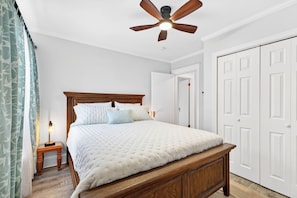 Une chambre avec un lit en bois, des murs blancs, un ventilateur de plafond et une porte blanche.