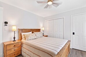 A bedroom with a wooden headboard, a bed with striped bedding, two bedside lamps, a nightstand with drawers, a ceiling fan, and white double doors. - Bright second-floor home with private deck, modern kitchen, and calm style. (Charlottetown)