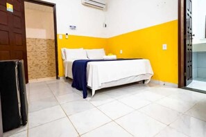 A hotel room with a bed, a door, a wall-mounted air conditioner, and a tiled floor. - POUSADA OASIS TROPICAL (CAIRU- MORRO DE SAO PAULO)