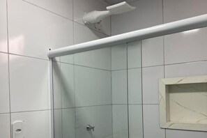 A shower area with white tiles, a glass door, and a white towel rack. - POUSADA OASIS TROPICAL (CAIRU- MORRO DE SAO PAULO)