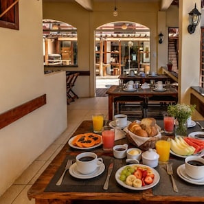 A breakfast table set with plates of fruit, coffee, and juice, with a view of the dining area in the background. - Oasis do Mar Inn (Cairu)