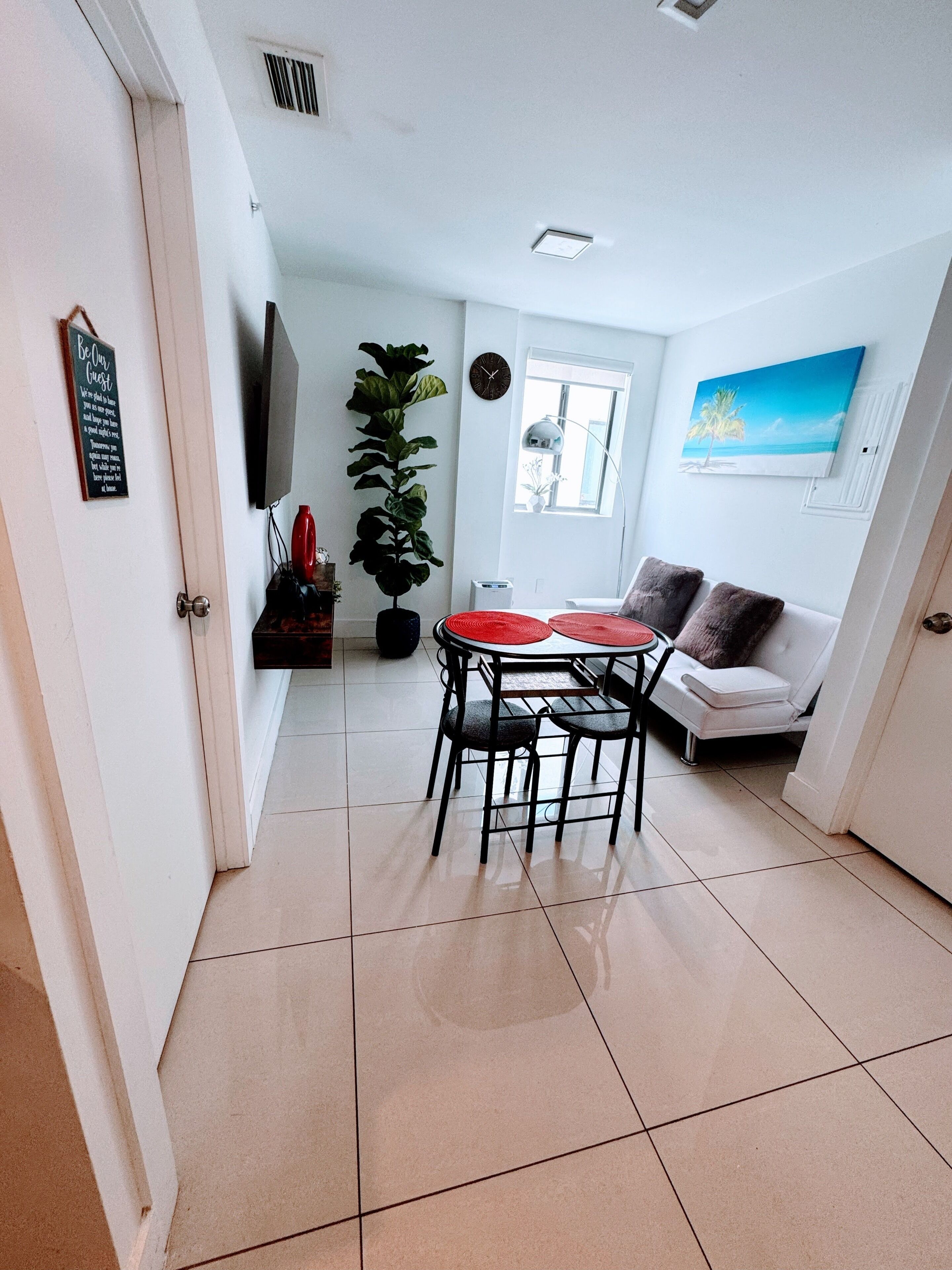 A living room with a dining table, a sofa, a potted plant, and a painting on the wall.