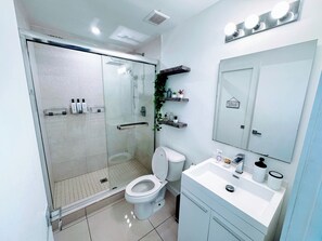 Une salle de bain moderne avec une douche à parois de verre, des toilettes, un lavabo avec un miroir et des étagères contenant des articles de toilette.
