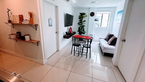 Un espacio habitable compacto con comedor, sofá, televisor y una planta.