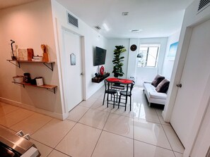 Un espace de vie compact comprenant un coin repas, un canapé, un téléviseur et une plante.