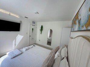 Une chambre à coucher comprenant un lit, un téléviseur à écran plat, un miroir et une œuvre d’art représentant une carte accrochée au mur.